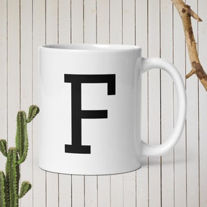 Può includere: Tazza in ceramica bianca con una lettera "F" nera stampata sul davanti.