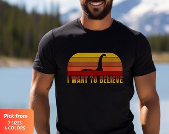 Może przedstawiać: Czarna koszulka z retro wzorem zachodu słońca przedstawiającym sylwetkę potwora morskiego i żółty napis "I WANT TO BELIEVE". Dostępna w 7 rozmiarach i 6 kolorach.