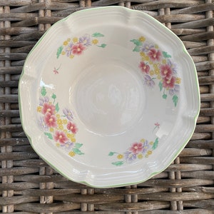May include: A white ceramic bowl with a green rim and a floral pattern. The bowl has a scalloped edge and features pink, purple, and yellow flowers.