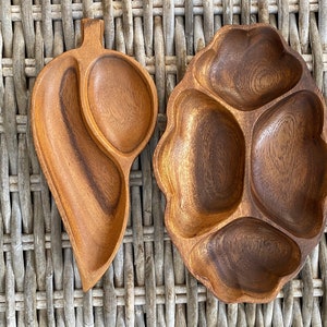 Pode incluir: Dois pratos de servir de madeira com vários compartimentos. O prato à esquerda tem a forma de uma folha e tem três compartimentos. O prato à direita é redondo e tem quatro compartimentos.