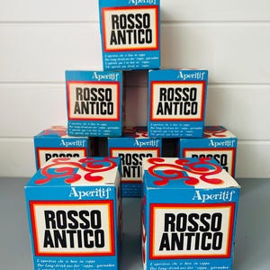 May include: A display of Rosso Antico aperitif boxes. The boxes, predominantly blue, feature a white and red label with the brand name. The boxes are arranged to highlight the product's branding.
