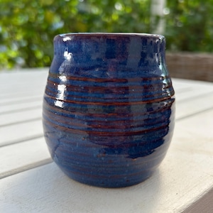 May include: A small, round, blue ceramic vase with brown stripes. The vase has a glossy finish.