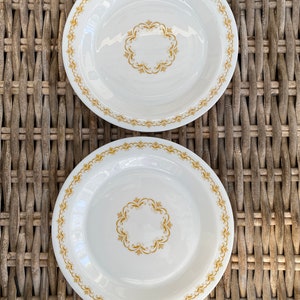 May include: Two white ceramic dinner plates with a gold rim and a gold floral design in the center.