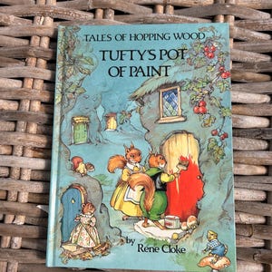 Puede incluir: Una portada de libro infantil vintage con un fondo azul e ilustraciones de ardillas pintando una puerta roja en un entorno de bosque de ensueño. El título es "Tales of Hopping Wood, Tufty's Pot of Paint" de Rene Cloke.