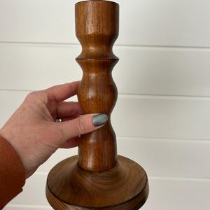 以下が含まれることがあります： 濃い茶色の木製キャンドルホルダー。キャンドルホルダーは、丸いベース、膨らんだ中間部、円筒形のトップを備えています。 木目は見えます。 ホルダーは、1本のろうそくを保持するように設計されています。