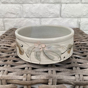 May include: A small, round, ceramic bowl with a light grey glaze and a hand-painted design of leaves and flowers in shades of green, brown, and pink.