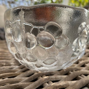 Puede incluir: Un cuenco de vidrio transparente con una superficie texturizada que se asemeja a uvas. El cuenco está sobre una superficie de mimbre tejido.