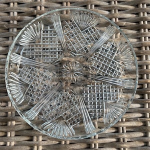 Puede incluir: Un plato para tartas de vidrio transparente con un patrón geométrico decorativo. El plato tiene un centro elevado y un borde festoneado.
