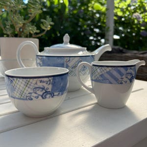 Puede incluir: Un juego de té de porcelana azul y blanco con una tetera, una jarra de crema y una taza de té. El juego presenta un diseño de patchwork con acentos florales.