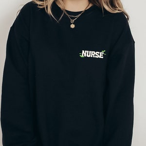 May include: Black sweatshirt with a green and white embroidered design that says "NURSE".