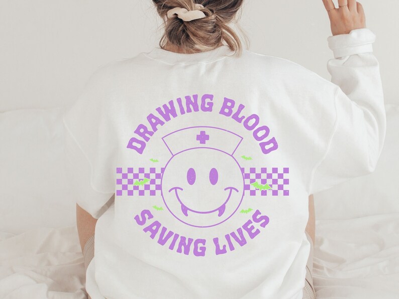 May include: White sweatshirt with a purple graphic design that says "Drawing Blood Saving Lives" with a purple smiley face with fangs and a nurse's hat.