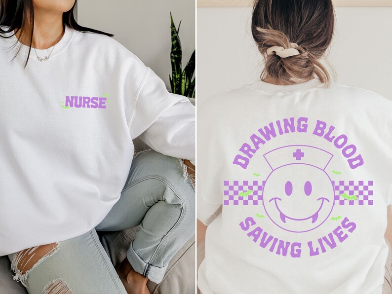 May include: White sweatshirt with a purple "NURSE" text on the front and a purple graphic on the back that says "DRAWING BLOOD SAVING LIVES" with a smiley face wearing a nurse's hat and a checkered pattern.