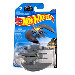 K&ouml;nnte beinhalten: Ein Hot Wheels Spielzeugauto des Batwing aus der Batman-Zeichentrickserie. Der Batwing ist dunkelgrau mit gelben Akzenten, verpackt auf einer blau-roten Karte. Die Verpackung enth&auml;lt die Logos von Hot Wheels und DC Comics.