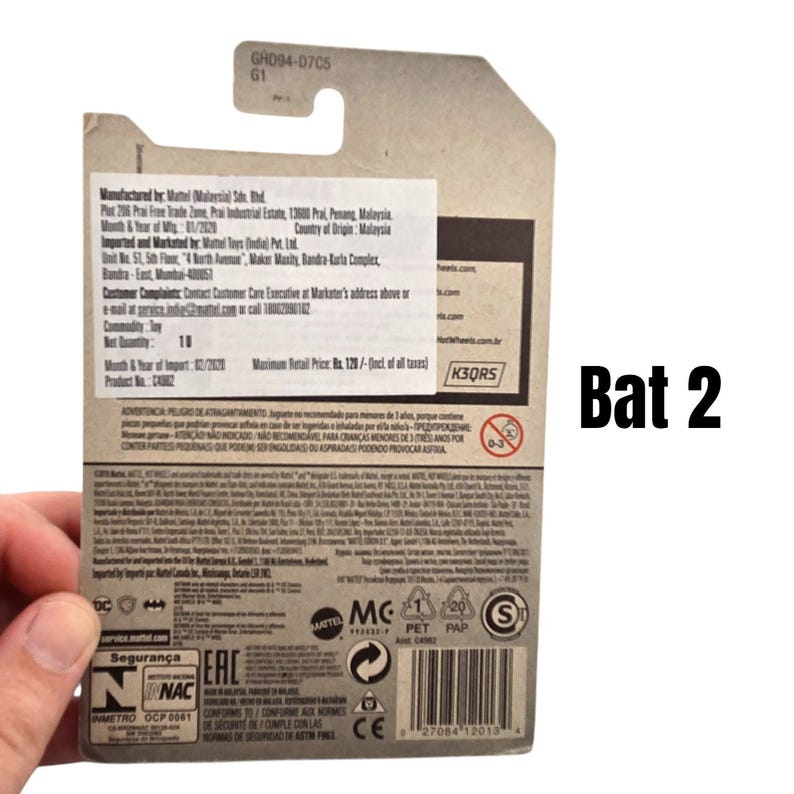 K&ouml;nnte beinhalten: Eine Hot Wheels Bat 2 Druckguss-Autoverpackung. Die Verpackung ist &uuml;berwiegend wei&szlig; mit schwarzem Text und Grafiken. Der Text "Bat 2" ist schwarz auf der rechten Seite der Verpackung aufgedruckt. Die Verpackung wird von einer Hand gehalten.