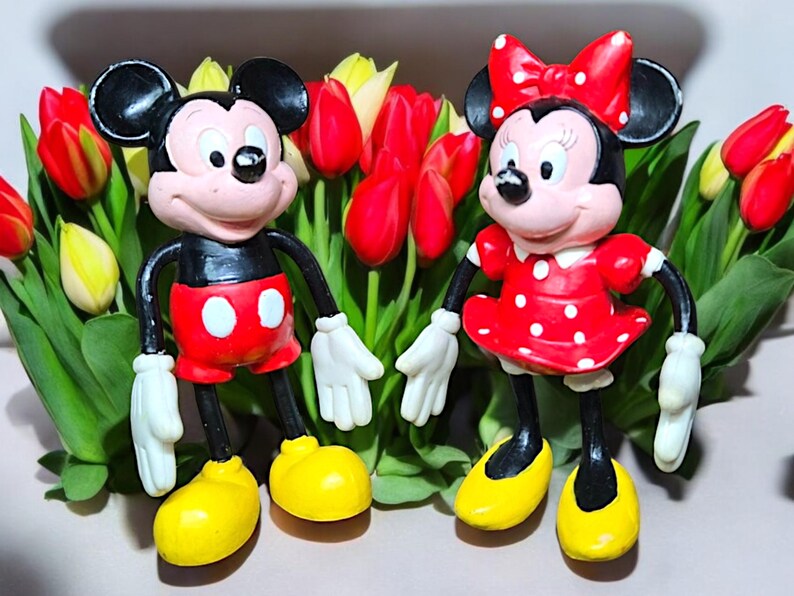 May include: A pair of vintage Mickey Mouse and Minnie Mouse figurines, both wearing red and white polka dot outfits. The figurines are standing in a bouquet of red and yellow tulips.