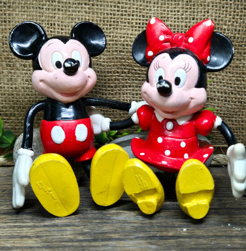 May include: A pair of vintage Mickey Mouse and Minnie Mouse figurines. Mickey is wearing red shorts with white polka dots and yellow shoes. Minnie is wearing a red dress with white polka dots and yellow shoes. Both figurines have black eyes and red noses.