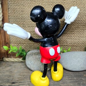 May include: A black and red plastic Mickey Mouse figurine with white gloves and yellow shoes. The figurine is standing with its arms raised and its head tilted back.
