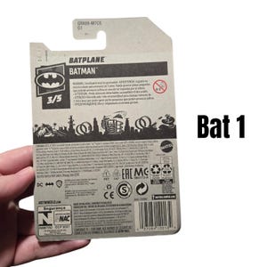 K&ouml;nnte beinhalten: Eine Hot Wheels Batplane Batman Spielzeugverpackung. Die Verpackung ist haupts&auml;chlich grau mit schwarz-wei&szlig;en Grafiken, einschlie&szlig;lich des Batman-Logos und dem Text "BATPLANE" und "BATMAN". Die Verpackung enth&auml;lt auch Sicherheitshinweise und einen Barcode.