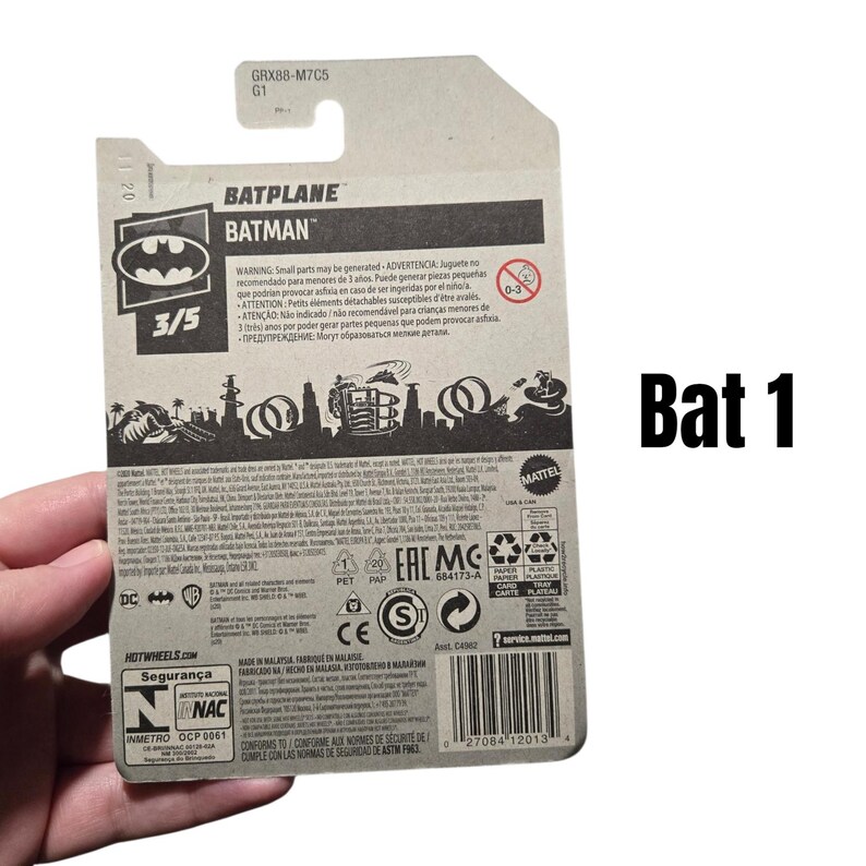K&ouml;nnte beinhalten: Eine Hot Wheels Batplane Batman Spielzeugverpackung. Die Verpackung ist haupts&auml;chlich grau mit schwarz-wei&szlig;en Grafiken, einschlie&szlig;lich des Batman-Logos und dem Text "BATPLANE" und "BATMAN". Die Verpackung enth&auml;lt auch Sicherheitshinweise und einen Barcode.