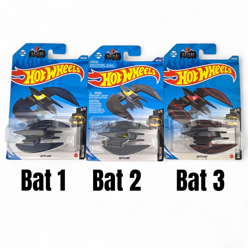 K&ouml;nnte beinhalten: Drei Hot Wheels Batplane Spielzeugautos auf blau-gelber Verpackung. Die Batplanes sind schwarz, grau und rot, mit gelben Akzenten. Die Verpackung enth&auml;lt das Batman-Logo und das Hot Wheels-Logo.