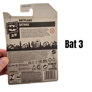 K&ouml;nnte beinhalten: Kartonverpackung f&uuml;r ein Hot Wheels Batplane-Spielzeug. Die Verpackung zeigt das Batman-Logo, den Text "BATPLANE BATMAN" und die Nummer "3/5". Die R&uuml;ckseite der Verpackung enth&auml;lt Sicherheitshinweise und einen Barcode.