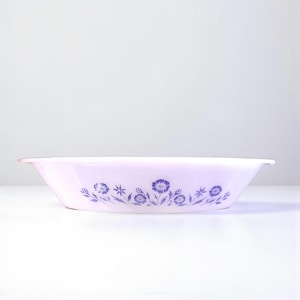 Peut inclure: Un plat de service ovale rose clair orné d'un motif floral violet. Le plat présente un bord légèrement évasé et est conçu pour servir des aliments. Le motif floral est répété autour du plat.
