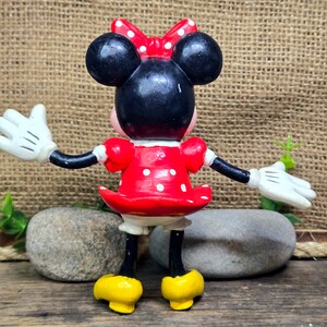 May include: A red and white polka dot dress with a black bow on top of the head. The figure is wearing white gloves and yellow shoes.