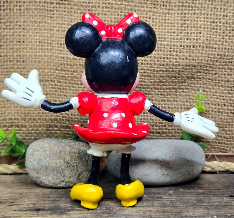 May include: A red and white polka dot dress with a black bow on top of the head. The figure is wearing white gloves and yellow shoes.