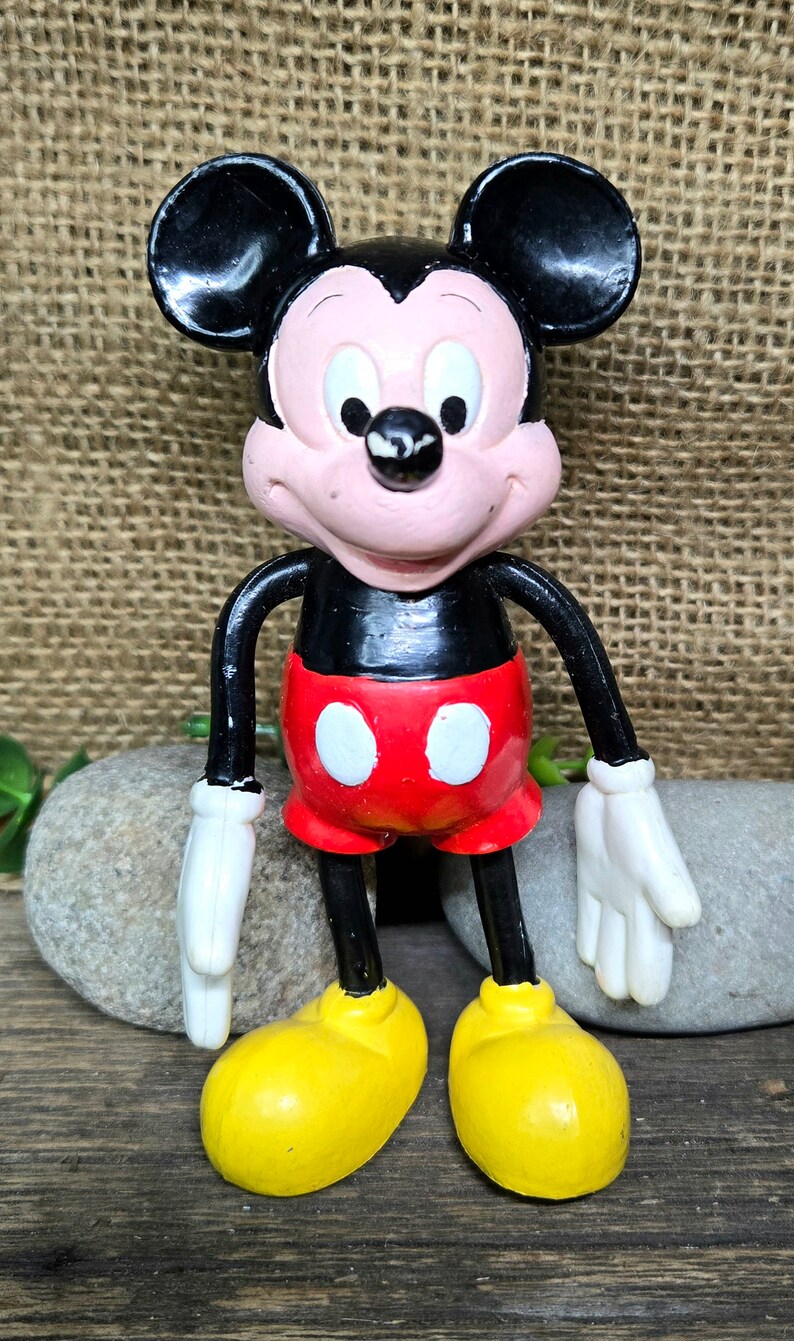 May include: A vintage plastic Mickey Mouse figurine with black ears, a black body, red shorts with white circles, yellow shoes, and a smiling face.