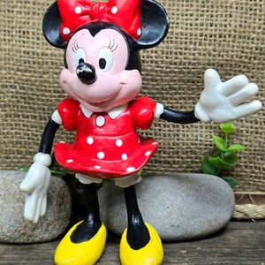 May include: A red and white polka dot dress with a black bow and white gloves. The figure is standing on a wooden surface with two gray rocks.