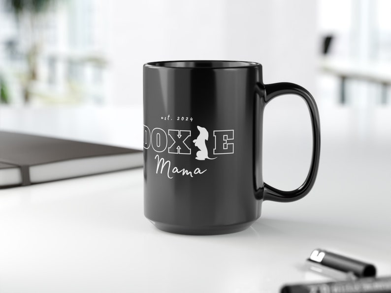 Black Doxie Mama mug with white lettering on a clean office desk.