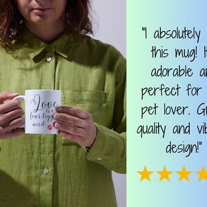May include: White ceramic mug with black text that reads "Love is a four-legged word" with two red paw prints. The mug is being held by a person wearing a green shirt.