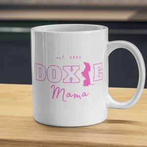 White Doxie Mama mug with pink lettering on a wooden kitchen counter.