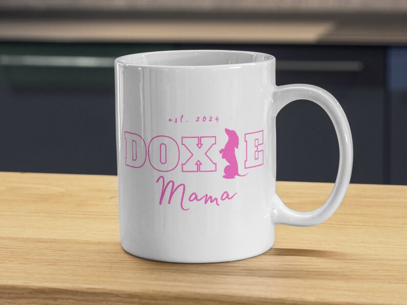 White Doxie Mama mug with pink lettering on a wooden kitchen counter.