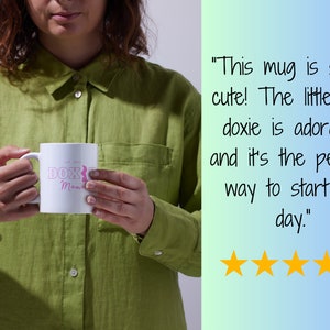 Customer holding a white Doxie Mama mug with pink lettering, alongside a positive review and five-star rating.