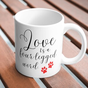 May include: White ceramic coffee mug with black text that reads "Love is a four legged word." Two red paw prints are below the text.