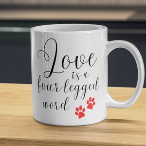 May include: White ceramic coffee mug with black text that reads "Love is a four legged word." Two red paw prints are below the text.