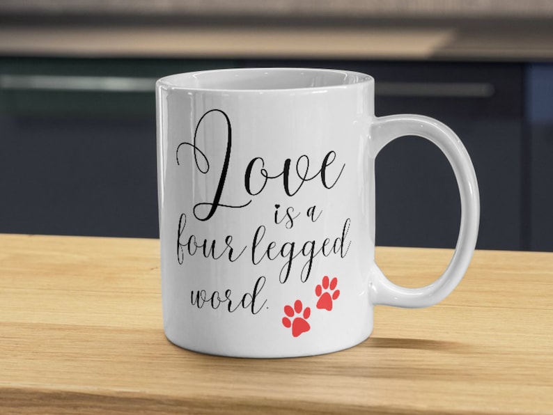 May include: White ceramic coffee mug with black text that reads "Love is a four legged word." Two red paw prints are below the text.