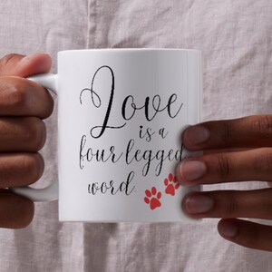 May include: White ceramic mug with black text that reads "Love is a four legged word" and two red paw prints.