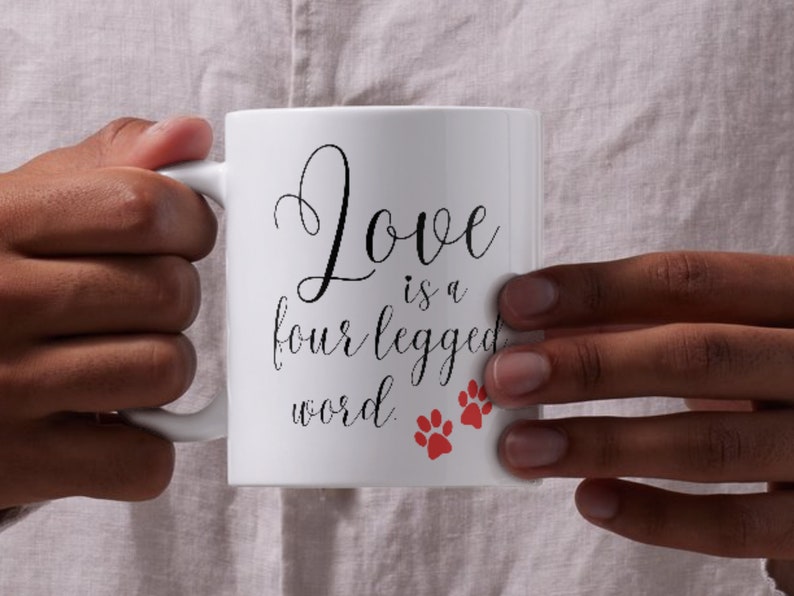 May include: White ceramic mug with black text that reads "Love is a four legged word" and two red paw prints.