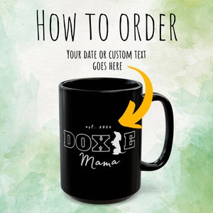 Black Doxie Mama mug with white lettering, highlighted with an arrow pointing to customization instructions.