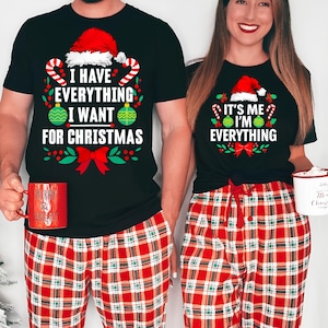 May include: Matching black Christmas t-shirts with festive text and graphics. One shirt reads "I HAVE EVERYTHING I WANT FOR CHRISTMAS," the other says "IT'S ME I'M EVERYTHING." Both wear red plaid pajama pants.