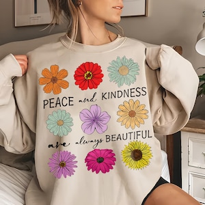 Peut inclure: Un sweat-shirt beige avec un imprimé graphique de fleurs colorées et le texte "Peace and kindness are always beautiful".