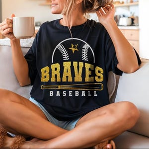 May include: A black t-shirt with a gold glitter design featuring a baseball, a star, and the words "BRAVES BASEBALL".