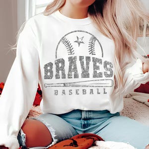 May include: White sweatshirt with a silver glitter design of a baseball, a star, and the word "BRAVES" with "BASEBALL" underneath.