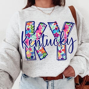 May include: A gray sweatshirt with a floral design of the letters "KY" and the word "Kentucky" in blue lettering.
