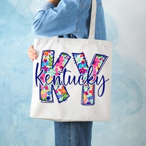 May include: A white tote bag with a floral design of the letters "KY" and the word "Kentucky" in blue script.