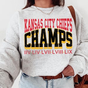 Può includere: Felpa grigia con il testo "Kansas City Chiefs Champs" in rosso, nero e giallo. Sotto il testo c'è "IV LIV LVII LVIII LIX" in giallo.