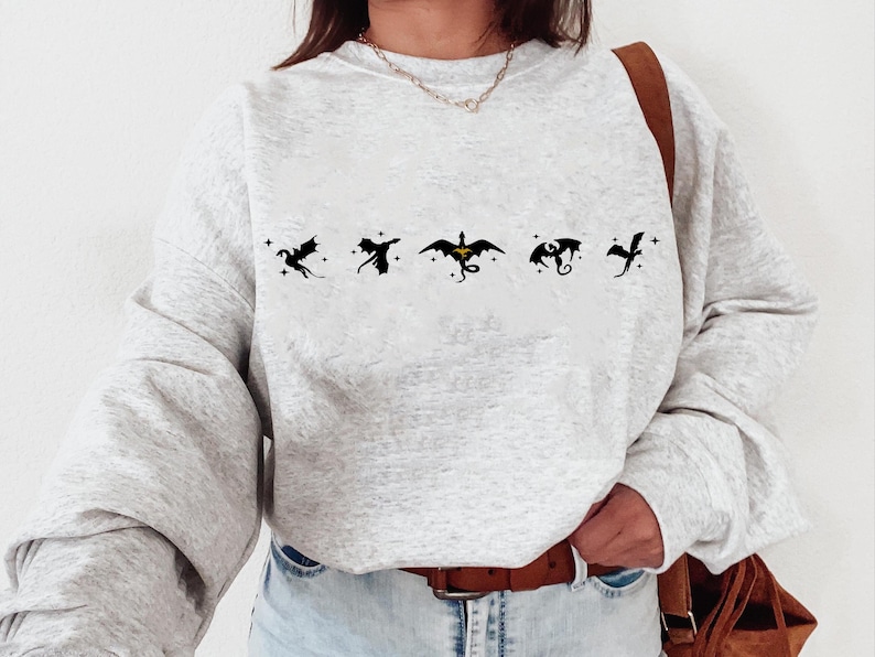 May include: A gray sweatshirt with a row of five black dragon silhouettes printed on the front. The dragons are flying in different directions, and the middle dragon has a yellow accent.