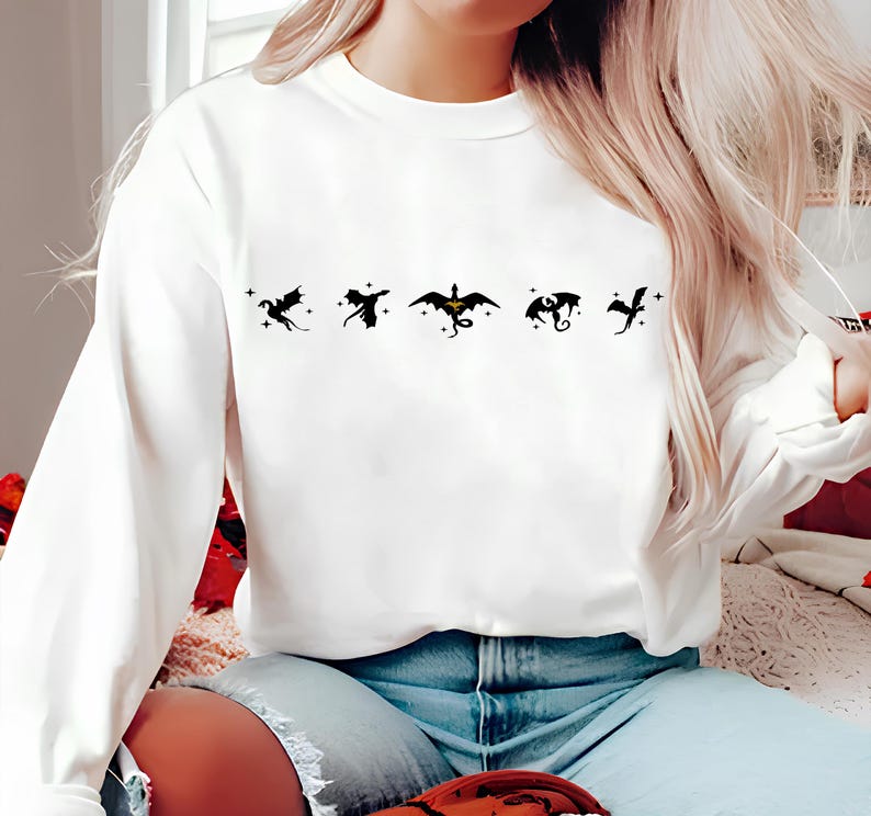 May include: White long-sleeve sweatshirt with a black graphic of five dragons. The dragons are in a row, facing right, with stars above them.